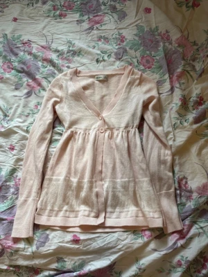 Söt rosa cardigan Hollister - En söt ljusrosa cardigan (ser mer beige ut i bild) i storlek Xs. Söta knappar och har en öppning vid magen. Nån defekt som kan förekomma är lite smuts eller små tecken på användning🌷