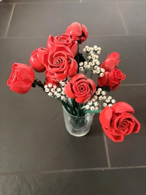 Bukett med LEGO-blommor  - Unik bukett byggd av LEGO-delar med röda rosor och små vita blommor. Blommorna står i en genomskinlig glasvas och är gjorda av plast. Perfekt som dekoration till skrivbordet eller som present till någon som gillar LEGO och kreativa detaljer. 11 röda, 4 vita!