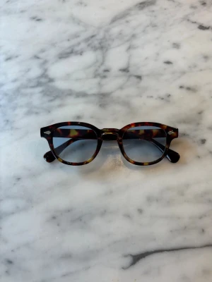 S&T 003 Brown solglasögon  - Snygga solglasögon med en riktigt stilig ram och där glaset är en blå nyans och gör att göasögenon får ett parfekt utseende. Dessa är även s&t mest populära glasögon så var snabba på att köpa 