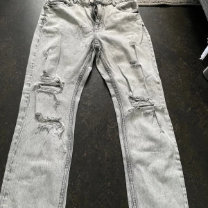 Grå slitna jeans med raka ben - Säljer ett par ljusgrå jeans med raka ben och flera slitningar framtill från bershka Jeansen har råa, fransiga benslut och klassisk femficksmodell. Perfekta för en avslappnad och trendig look.