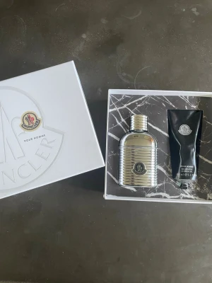 Moncler parfymset - Lyxigt parfymset från Moncler med en silverfärgad parfymflaska (60ml) och en svart duschgel-tub (100ml). Knappt använda, ca 90% är kvar. Levereras i en elegant vit presentask.