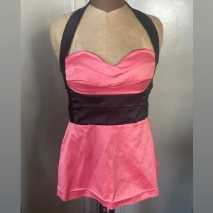 Rosa och svart halterneck tubtopp - Snygg tvåfärgad tubtopp i rosa och svart med halterneck-band och markerad midja. Toppen har vadderad byst, dragkedja bak och lätt utsvängd nederdel. Innesidan är vadderad. Storlek eur 38