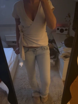 Vit omlottopp med knyt - Vit omlottopp med kort ärm och knyt i sidan. Toppen har djup v-ringning och croppad passform som ger en trendig och fräsch look. Perfekt att matcha med jeans eller kjol. Troligen i mjuk bomull eller bomullsblandning.