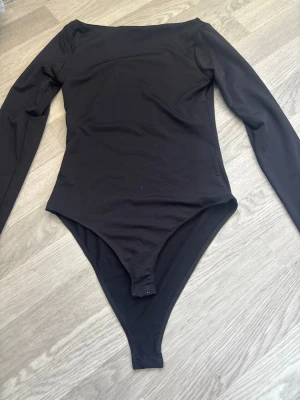 Svart långärmad body - En stilren svart body med långa ärmar och rund halsringning. Bodyn har tryckknappar i grenen för enkel på- och avtagning. Tillverkad i ett stretchigt och mjukt material som sitter tajt mot kroppen. Perfekt att matcha med jeans eller kjol.