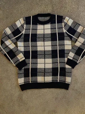 Zara - Snygg stickad tröja i svart och vitt med rutigt mönster. Tröjan har rund halsringning och långa ärmar. Perfekt för dig som gillar klassiska mönster med en modern twist.