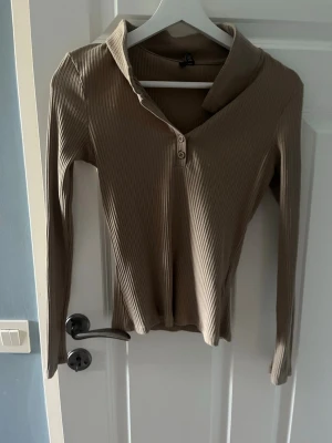 Beige ribbad långärmad topp - Snygg beige ribbad topp med lång ärm och v-ringning med två knappar framtill. Toppen har en mjuk krage och är figurnära i modellen, perfekt att styla med jeans eller kjol.