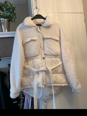 Beige pufferjacka med teddy och bälte - Snygg vit pufferjacka från Pieces med teddy-detaljer på ärmar och axlar. 