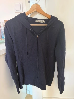 Mörkblå hoodie från William de Faye - Mörkblå hoodie med dragkedja från William de Faye. Modellen har huva med dragsko och långa ärmar. Tillverkad i mjukt material som känns skönt mot huden. Perfekt för en avslappnad och stilren look.