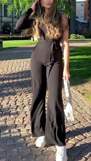Svart omlott jumpsuit med utsvängda ben - Trendig svart jumpsuit med omlott-skärning och långa ärmar. Utsvängda ben och knytskärp i midjan ger en snygg siluett. Perfekt för dig som gillar stilrena och bekväma plagg. Materialet ser ut att vara mjukt och stretchigt.