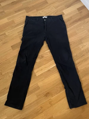 Svarta chinos från NN07 - Snygga svarta chinos från NN07 med klassisk rak passform. Byxorna har framfickor, två bakfickor och stängs med knapp och dragkedja. Perfekta för en stilren look och tillverkade i mjukt bomullstyg. Tillverkade i Italienskt tyg. Dom är små i storleken.