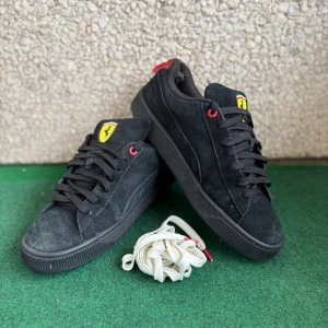 Svarta Puma Ferrari sneakers i mocka - Svarta sneakers från Puma i samarbete med Ferrari. Skorna är i mocka med svarta sulor, svarta skosnören och röda detaljer. Ferrari-logga på plösen och extra vita skosnören medföljer. Snygg och sportig modell med låg profil.
