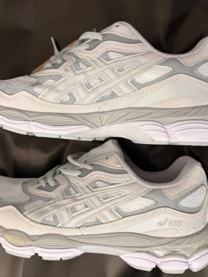 Vita och grå Asics sneakers - Snygga sneakers från Asics i vitt och ljusgrått med mesh och syntetmaterial. Skorna har klassisk låg profil, bekväm dämpning och ikoniska Asics-loggan på sidan. Perfekta för dig som gillar stilrena och sportiga skor.