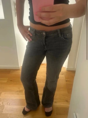 Grå bootcut jeans med låg midja - Säljer ett par grå bootcut jeans med låg midja och klassiska fem fickor. Jeansen har en lätt tvättad look och raka ben som går ut lite nedtill. Perfekta för dig som gillar en avslappnad men ändå snygg stil. Materialet är mjukt denim i bomull.
