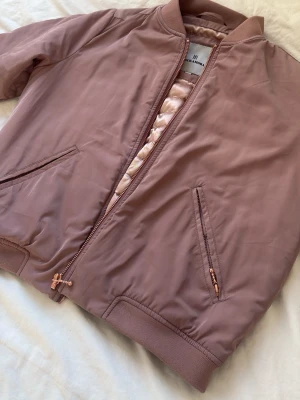 Rosa bomberjacka från Rockandora - Snygg bomberjacka i dammigt rosa från Rockamora. Jackan har glansigt foder, ribbade muddar och dragkedja framtill. Två snedställda fickor med dragkedja och klassisk bomberkrage. Perfekt för våren💞 Använd en gång. SKRIV ANGÅENDE FRAKT