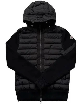 Svart Moncler pufferjacka med huva - Svart pufferjacka från Moncler med stickade ärmar och ribbade muddar. Jackan har huva, tvåvägsdragkedja och en ficka med dragkedja på ärmen. Materialmix av polyester och stickad ull ger en schysst look. Perfekt för dig som gillar streetstyle.