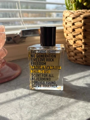 Zadig & Voltaire This Is Us! parfym - En stilren parfymflaska från Zadig & Voltaire med svart lock och transparent glas. Flaskan har modern text i svart och gult på framsidan. Doften heter 'This Is Us!' och passar dig som gillar en ungdomlig och fri känsla. 30ml. Se bild hur mycket som använts 