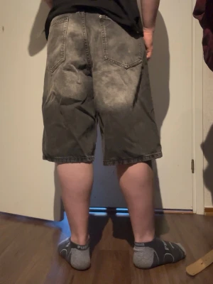 Grå baggy denimshorts - Säljer ett par grå denimshorts med slitna detaljer och femficksmodell. Shortsen har en loose passform och går ner till knäna. Klassisk design med bälteshällor och synliga sömmar. Perfekta för en avslappnad stil.
