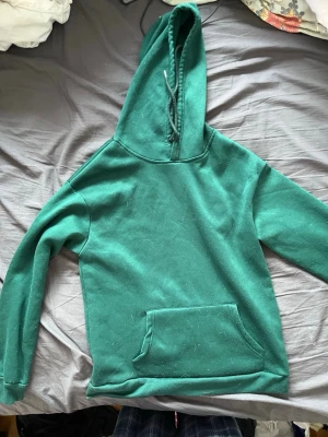 Grön hoodie från SHEIN med ficka - Enkel grön hoodie från SHEIN i 100% polyester. Klassisk modell med stor huva, dragsko och en rymlig magficka. Perfekt för chill dagar eller när du vill ha en avslappnad stil. Mjuk insida och långa ärmar. Lite lite nopprig men knappt något som märks.