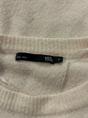 Vit stickad tröja från 157 - Vit stickad tröja från 157 med korta ärmar och rund halsringning. Tröjan har en enkel och stilren design med ribbstickade muddar vid ärmslut och hals. Perfekt för lager-på-lager och passar till många olika outfits.