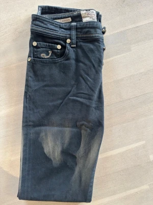 Mörkblåa jeans från Jacob Cohen - Snygga mörkblå jeans från Jacob Cohen med klassisk femficksdesign och dekorativ J-detalj på myntfickan. Jeansen har knäppning med silverfärgade knappar och kontrastsömmar. Materialet är mjukt denim i bomull med lätt tvättad look.