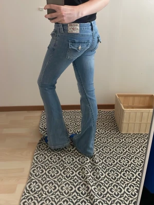 Ljusblå bootcut jeans True Religion - Säljer ett par ljusblå bootcut jeans från True Religion med klassiska kontrastsömmar och fickdetaljer med lock och knapp bak. Jeansen har en snygg tvätt och utsvängda ben, perfekta för en avslappnad och trendig look.