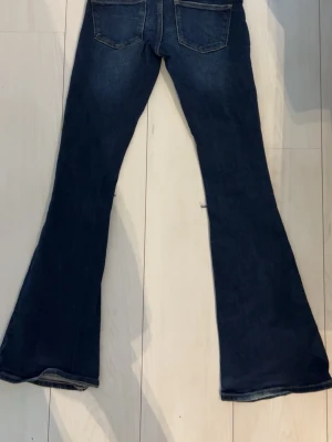 Mörkblå utsvängda jeans med slitningar - Snygga mörkblå jeans med utsvängda ben och slitna detaljer på framsidan. Jeansen har klassiska bakfickor och framfickor, samt låg midja. Perfekta för en trendig och avslappnad stil.