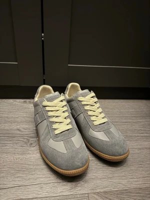 Grå sneakers från Maison Margiela - Säljer ett par maison margiela gats I storlek 41, skorna är i nytt skick och box och dustbugs medföljer. Hör av er vid eventuella funderingar!