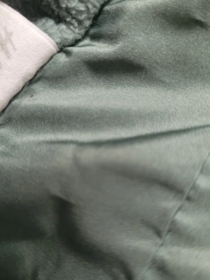 Grön jacka med Musse Pigg-motiv - Snygg grön jacka med huva och tryck av Musse Pigg över hela jackan. Jackan har elastiska muddar och är tillverkad i ett lätt, vindtätt material. Perfekt för dig som gillar Disney och vill ha en lekfull stil.