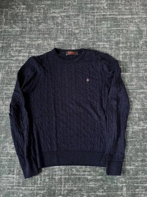 Mörkblå kabelstickad tröja Morris - Kabelstickad mörkblå tröja från Morris i 100% merinoull. Rund halsringning, långa ärmar och diskret logga broderad på bröstet. Perfekt för dig som gillar klassisk och stilren design.