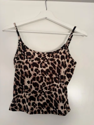 Leopardmönstrad linnetopp - Säljer en snygg leopardmönstrad linnetopp med tunna axelband. Toppen har en beige och svart färgkombination och är perfekt för dig som vill sticka ut. Materialet känns mjukt och följsamt mot huden.