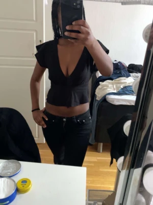 Svart croppad v-ringad topp - Snygg svart croppad topp med djup v-ringning och korta ärmar. Perfekt för dig som vill ha en enkel men ändå trendig look. Toppen har en figurnära passform och är lätt att matcha med olika stilar.