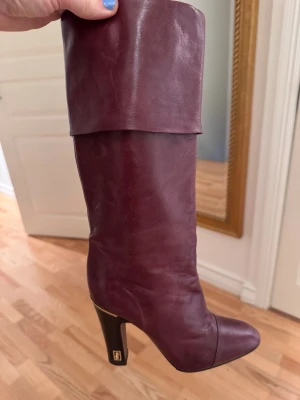 Vinröda läderstövlar från Marc Jacobs - Snygga vinröda stövlar i äkta läder från Marc Jacob med hög klack och rundad tå. Stövelskaftet är högt och kan vikas ner för en cool look. Klacken har en gulddetalj. Perfekta för att lyfta din outfit. Nysulade. 