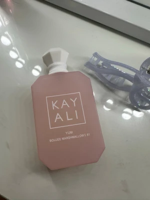 Kayali Yum Boujee Marshmallow 81 parfym - Säljer en Kayali Yum Boujee Marshmallow 81 parfym i en matt ljusrosa flaska med vit, geometrisk kork. Flaskan har en modern, kantig form och är tillverkad i glas. Perfekt för dig som gillar söta och unika dofter.