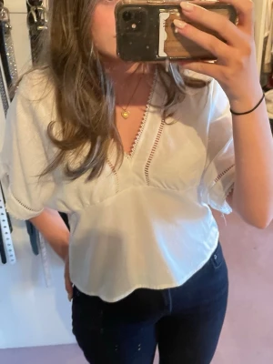 Vit v-ringad blus - Söt vit blus köpt på missäy med v-ringning och dekorativa spetsdetaljer längs halsringning och ärmslut. Blusen har korta, vida ärmar och en avslappnad passform. Endast använd av mig fåtal gånger och precis som ny. Den är i storlek S/M så passar båda!! Hör av er vid frågor/intresse💞