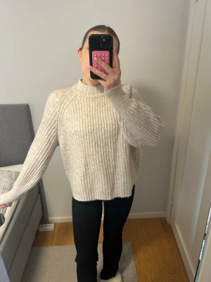 Beige ribbstickad tröja med hög krage - Säljer en beige ribbstickad tröja med hög krage och långa ärmar. Tröjan har en avslappnad passform och är gjord i ett mjukt stickat material som är perfekt för kyliga dagar. Passar dig som gillar en enkel och stilren look.