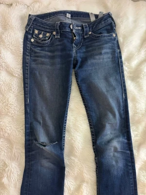 True Religion blå bootcut jeans - Supersnygga blå bootcut jeans från True Religion med lite slitningar slitningar och ett hål på höger ben. Bortsett från det är de i jätte fint skick. 💞