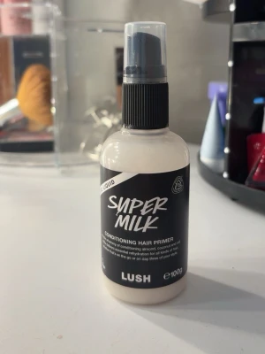 Lush Super Milk Conditioning Hair Primer - Super Milk Conditioning Hair Primer från Lush är en vit, flytande leave-in spray för håret. Innehåller mandel-, kokos- och havremjölk som återfuktar och reder ut håret. Kommer i en rund plastflaska med svart spraymunstycke, 100g.