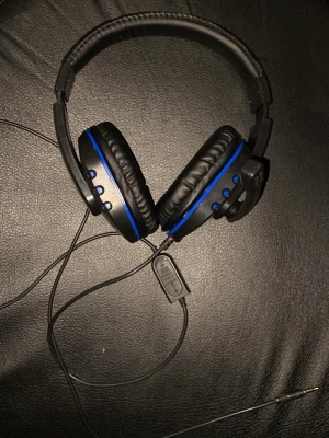 Svarta gaminghörlurar med blå detaljer - Snygga over-ear gaminghörlurar i svart med blå detaljer och vadderade kåpor. Utrustade med justerbar mikrofon och kabel med volymkontroll. Perfekta för gaming eller videosamtal. Tillverkade i plast och konstläder.