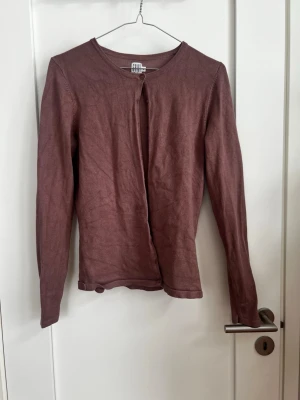 Brun,röd kofta - Säljer en tunn, långärmad brun kofta Koftan har rund halsringning och stängs med knappar upptill. Enkel och stilren design i mjukt material, perfekt att slänga över en topp eller klänning.