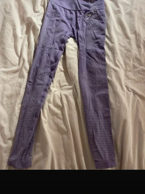 Lila seamless leggings från Gymshark - Säljer ett par lila seamless leggings från Gymshark. Stretchigt material som sitter tajt och bekvämt, perfekt för träning och gymmet. Gymshark-logga på höften och vristen för en sportig vibe.