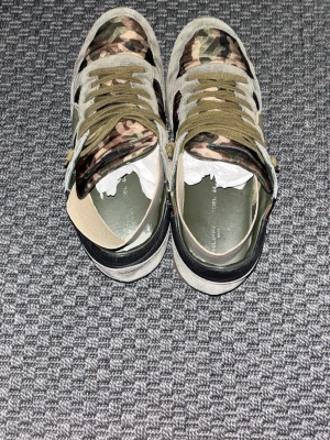 Camo sneakers från Philippe Model - Snygga sneakers från Philippe Model med camouflagemönster i grönt, brunt och beige. Skorna har olivgröna skosnören, detaljer i mocka och läder samt en robust sula. Perfekta för dig som vill sticka ut med en streetwear-look.