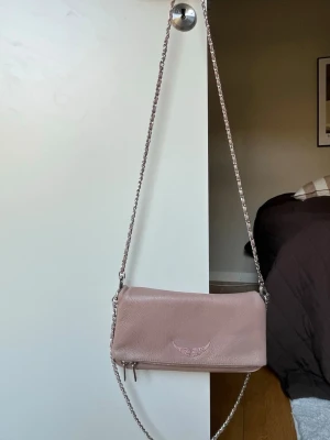 Rosa axelväska från Zadig & Voltaire - Säljer denna sparsamt använda Zadig väska i en jätte fin puder rosa färg, den har inga defekter förutom att kedjan har rostat lite (se sista bilden), vilket man inte märker av, märkte först när jag skulle gå igenom den! Måtten är ish: längd 25cm, höjd 10cm. Den är den större storleken. Äkthetsbevis finns och skickas med.