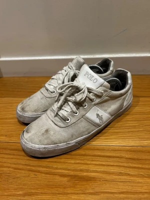 Polo Ralph Lauren sneakers *42* - Snygga vita sneakers från Polo Ralph Lauren med klassisk låg profil och ikoniska loggan på sidan. Skorna har vita snören, metallöljetter och ovandel i canvas med detaljer i läder. Perfekta för en clean och stilren look.