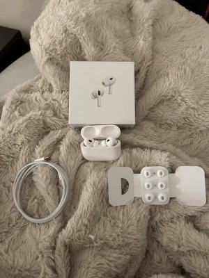 Apple AirPods Pro 2 - Säljer ett par vita Apple AirPods Pro2 med trådlöst laddningsetui. In-ear-modell med silikonproppar i flera storlekar, brusreducering och touchkontroller. Levereras med originalkartong, laddningskabel och extra öronproppar. Snygg och stilren design i plast.
