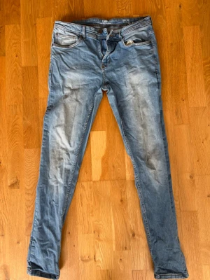 Blå slim jeans i klassisk modell - Snygga blå jeans med slim passform och klassisk femficksdesign. Jeansen har en ljus tvätt med slitningar framtill och är tillverkade i bomull. Perfekta för en avslappnad och trendig stil.