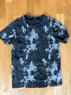 Svart t-shirt med mönster Jack & Jones - Cool svart t-shirt från Jack & Jones Premium med unikt grått och vitt batikmönster och stänkdetaljer. Rund halsringning och korta ärmar. Perfekt för en avslappnad och trendig stil.