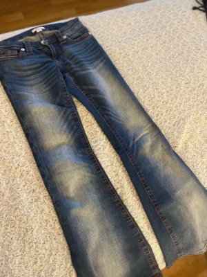 Blå bootcut jeans med slitningar - Säljer ett par blå bootcut jeans med snygga slitningar och kontrastsömmar. Jeansen har klassisk femficksdesign och detaljerade bakfickor med broderi. Perfekta för en avslappnad och trendig look. Materialet är denim i bomull. Pris kan diskuteras! Kontakta mig vid frågor💕