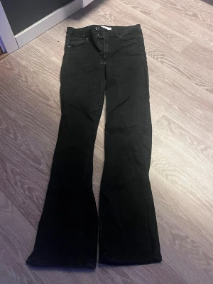 Svarta bootcut jeans - Snygga svarta bootcut jeans med klassisk femficksdesign och normal midja. Jeansen har utsvängda ben och stängs med knapp och dragkedja. Perfekta för dig som vill ha en tidlös och trendig look.
