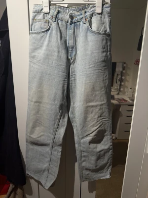 Ljusblå raka jeans med rå kant - Säljer ett par ljusblå jeans från Gina Tricot med rak passform och råa, avklippta benslut. Jeansen har klassisk femficksdesign, bälteshällor och gylf med dragkedja. Perfekta för en avslappnad och trendig look.