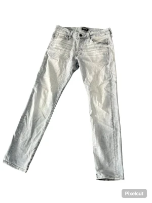Ljusgrå jeans från Jack & Jones - Snygga ljusgrå jeans från Jack & Jones med klassisk femficksdesign och raka ben. Jeansen har bälteshällor och knappgylf. Perfekta för en avslappnad och trendig stil.